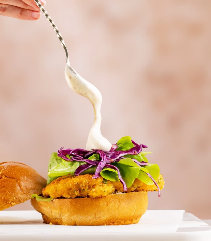 Creamy sauce being drizzled over a fresh burger to showcase bespoke product development and flavour innovation.