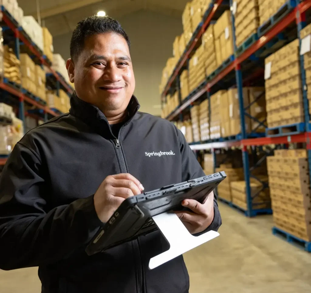 Springbrook team member in warehouse using tablet among stacked boxes